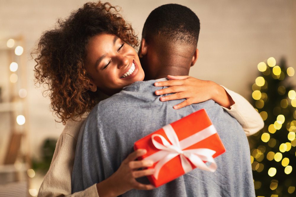 Woman in a tan sweater receiving a med spa christmas gift hugging husband at home