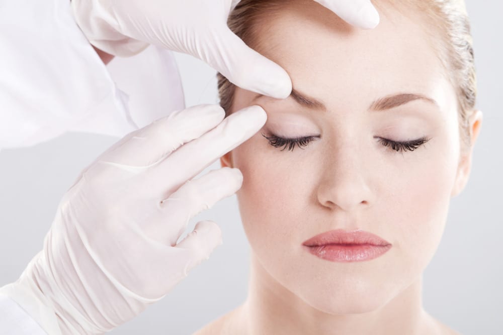 Brow lift benefits concept. Closup of a woman's face as her eyes are closed while a facial plastic surgeon evaluates her brow.
