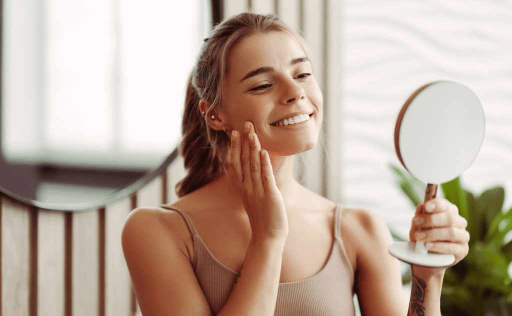 Smiling woman checking her healed skin in a hand mirror